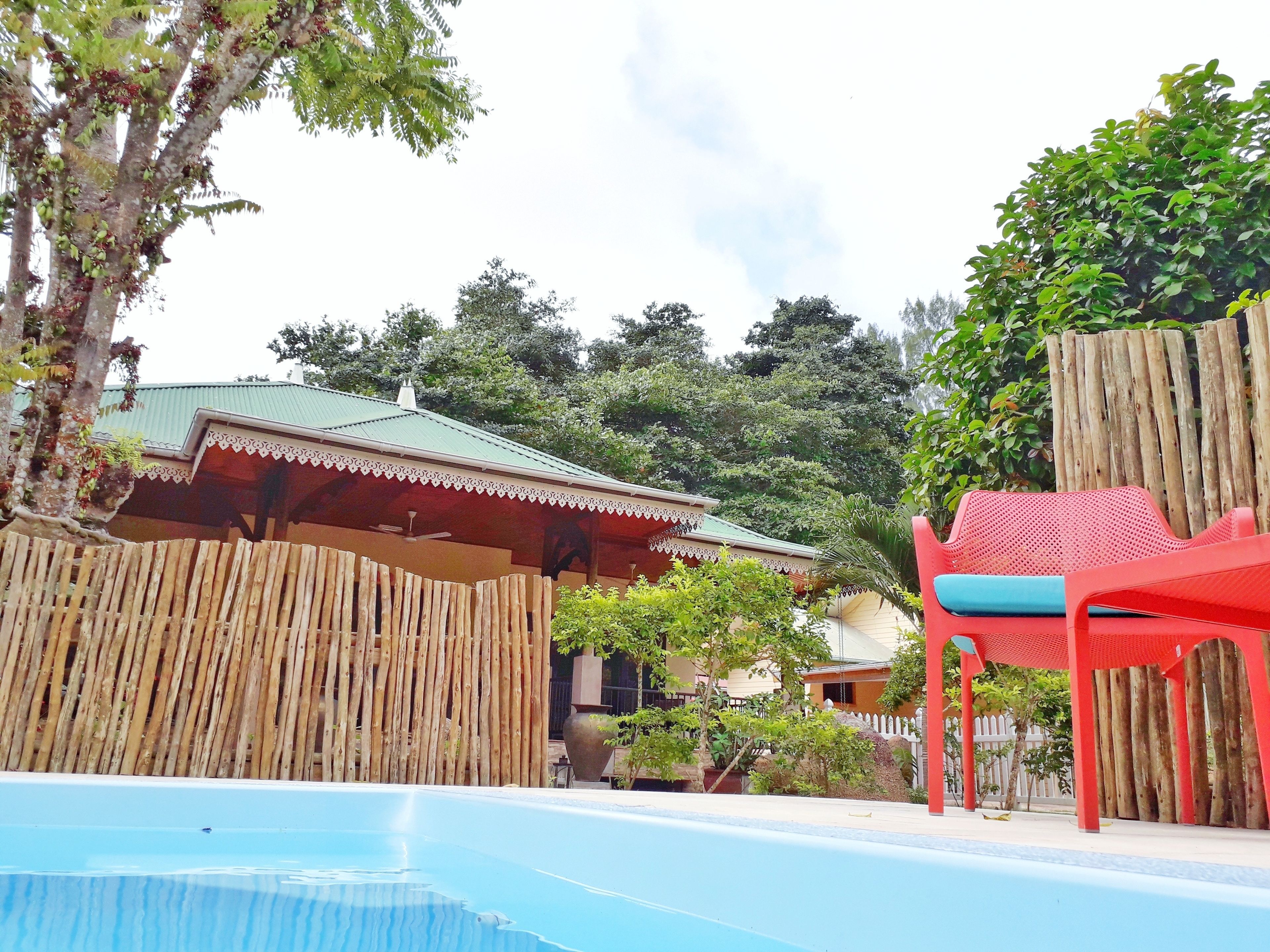 A pool area with a bamboo fence, a red chair, and a building with a green roof.