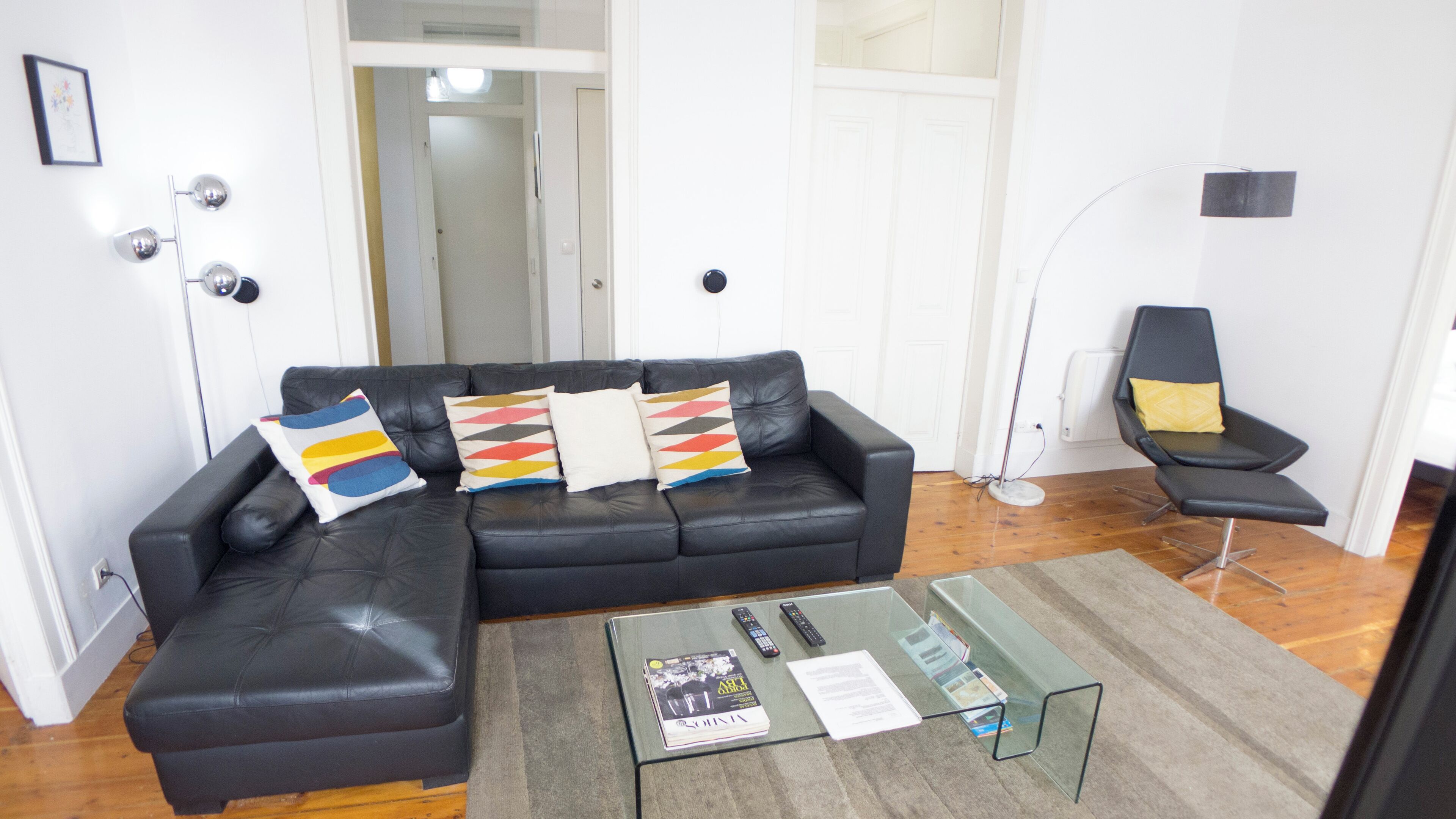 Una sala de estar con un sofá de cuero negro, una mesa de centro de vidrio y un sillón negro.