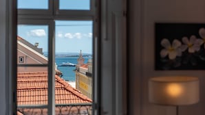 Vista a través de una ventana con techo de tejas, una lámpara y un cuadro con flores.