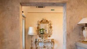 A hallway with a mirror, a console table with a vase of flowers, and a lamp. - Hotel Della Rosa (Ancona)