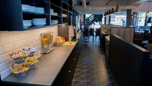 A modern kitchen with a long counter, various food items, and a view of the dining area. - Systra Hotel Apartments Sjøholt (Ålesund)