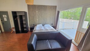 A room with a large bed, a black sofa, a wooden floor, a wardrobe, and a view of a balcony with a railing. - Systra Hotel Apartments Sjøholt (Ålesund)