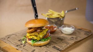 A burger with a knife on top, fries, and two dipping sauces on a newspaper-lined surface. - Systra Hotel Apartments Sjøholt (Ålesund)