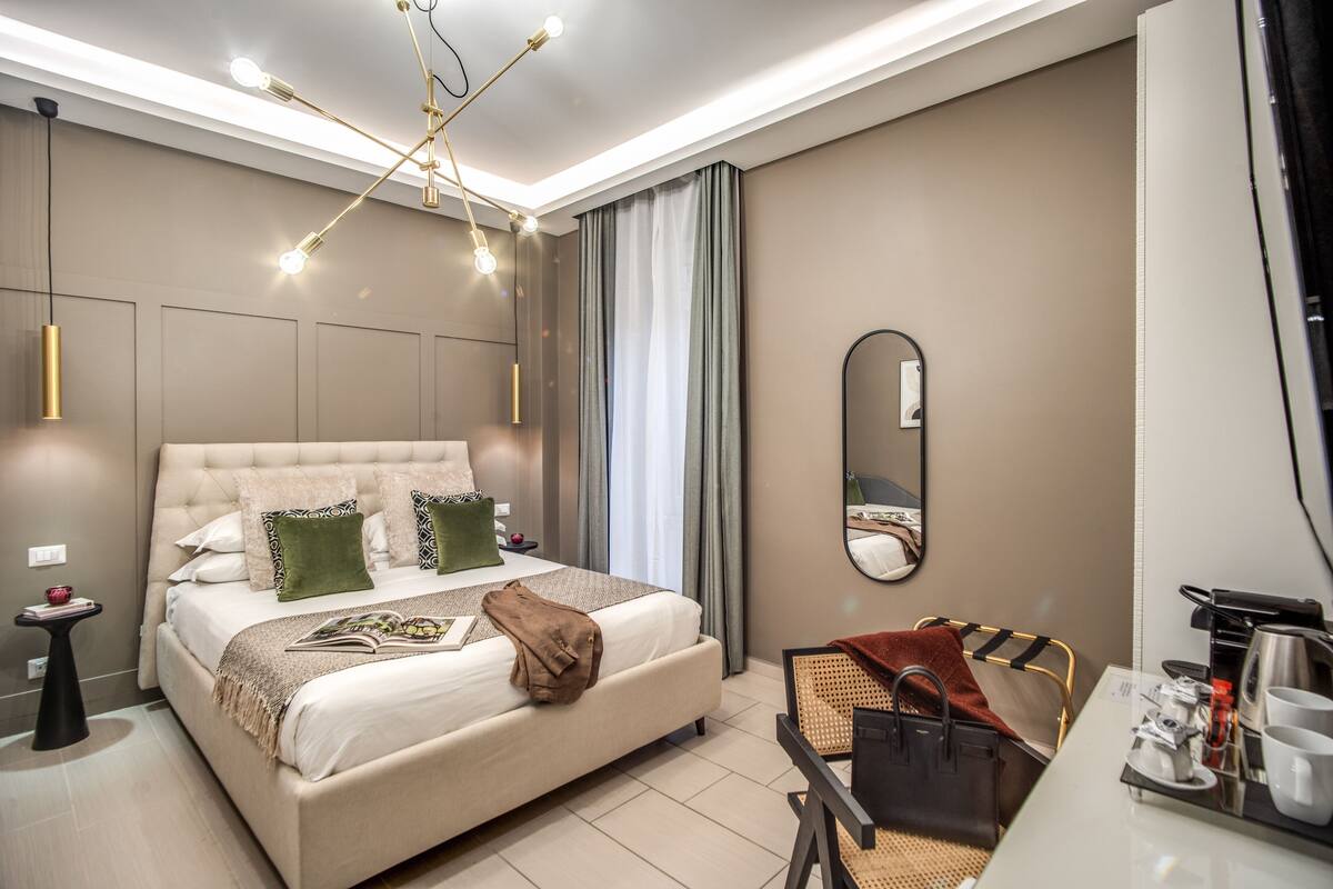 A modern hotel room with a large bed, bedside tables, a desk, and a mirror.
