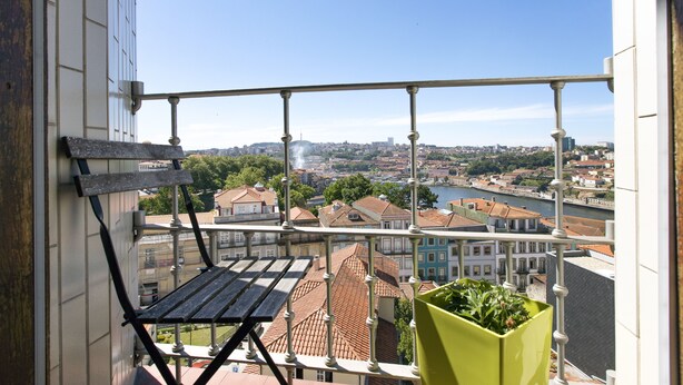 A balcony with a view of a cityscape, a wooden bench, and a green planter.