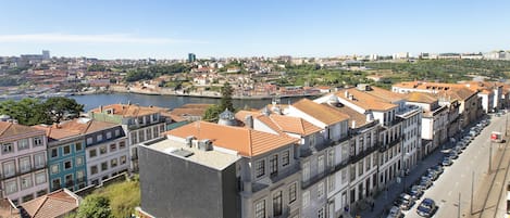 A row of traditional European buildings with red-tiled roofs, a river in the background, and a clear sky.
