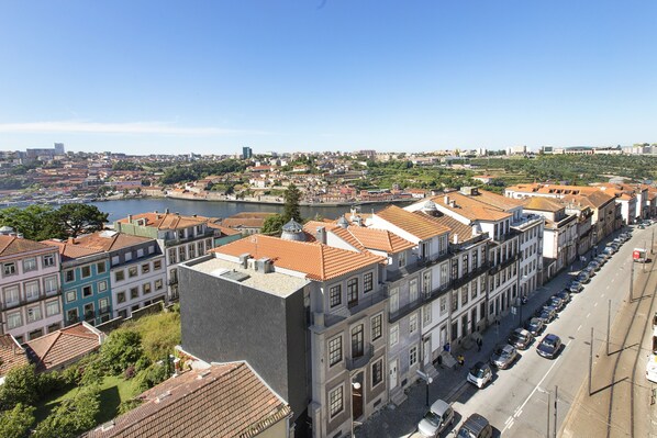 A row of traditional European buildings with red-tiled roofs, a river in the background, and a clear sky.