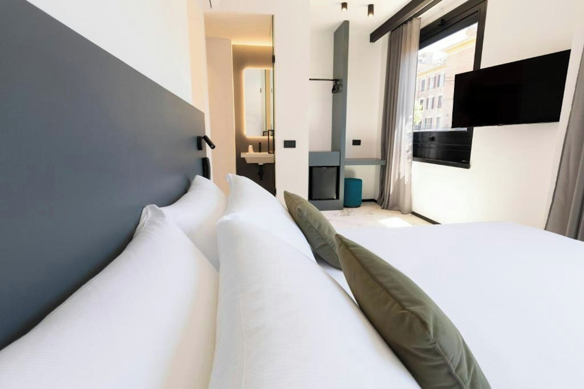 Habitació d'hotel amb un llit, una televisió, una finestra i un bany al fons.