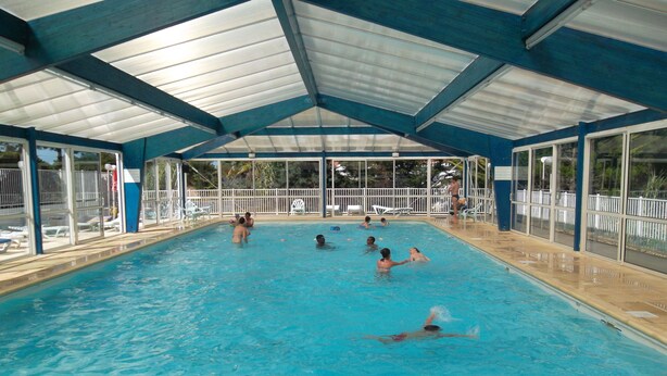 An indoor swimming pool with clear glass walls, a blue roof, and a tiled floor. - le Hameau de l'Océan (Saint-Hilaire-de-Riez)