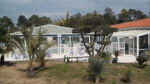 A glass-roofed building with a white exterior, surrounded by palm trees and other vegetation. - le Hameau de l'Océan (Saint-Hilaire-de-Riez)