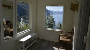 Habitación con un ventanal grande que ofrece vistas a un lago y montañas. Incluye una silla de madera y un banco blanco.