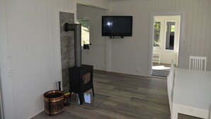 Una habitación con estufa de leña, televisor montado en la pared y una mesa de comedor blanca.