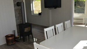 Una habitación con estufa de leña, televisor montado en la pared y una mesa de comedor con sillas.