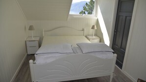 Un dormitorio con cama blanca, dos mesitas de noche, una ventana con vistas y una puerta oscura.