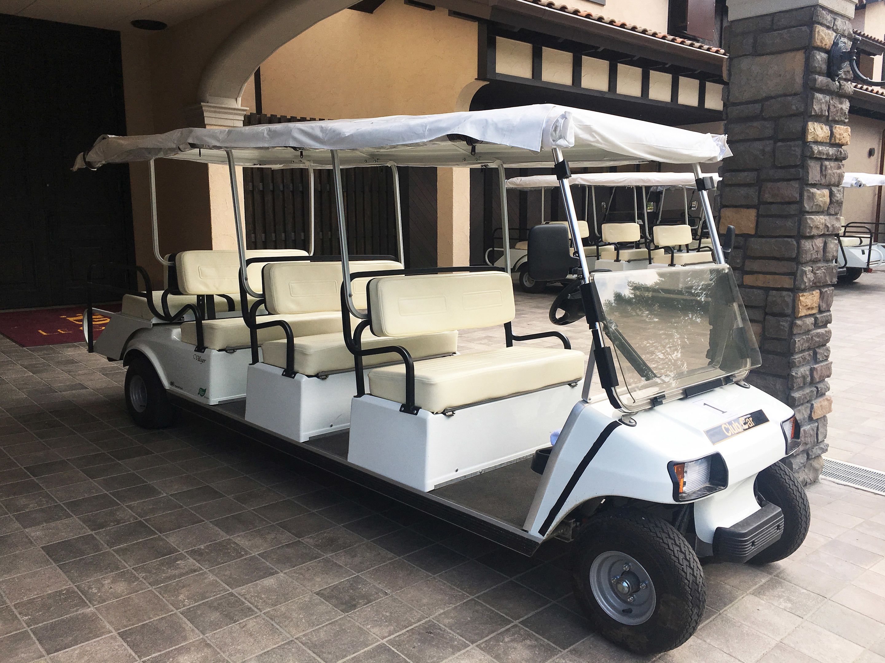 Un carrito de golf con toldo, estacionado frente a un edificio con pilares de piedra y piso de baldosas.