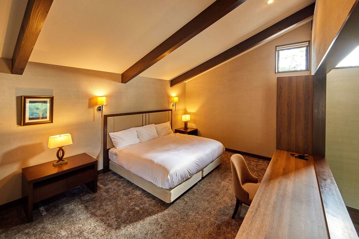 A hotel room with a bed, bedside tables, a desk, and a chair.