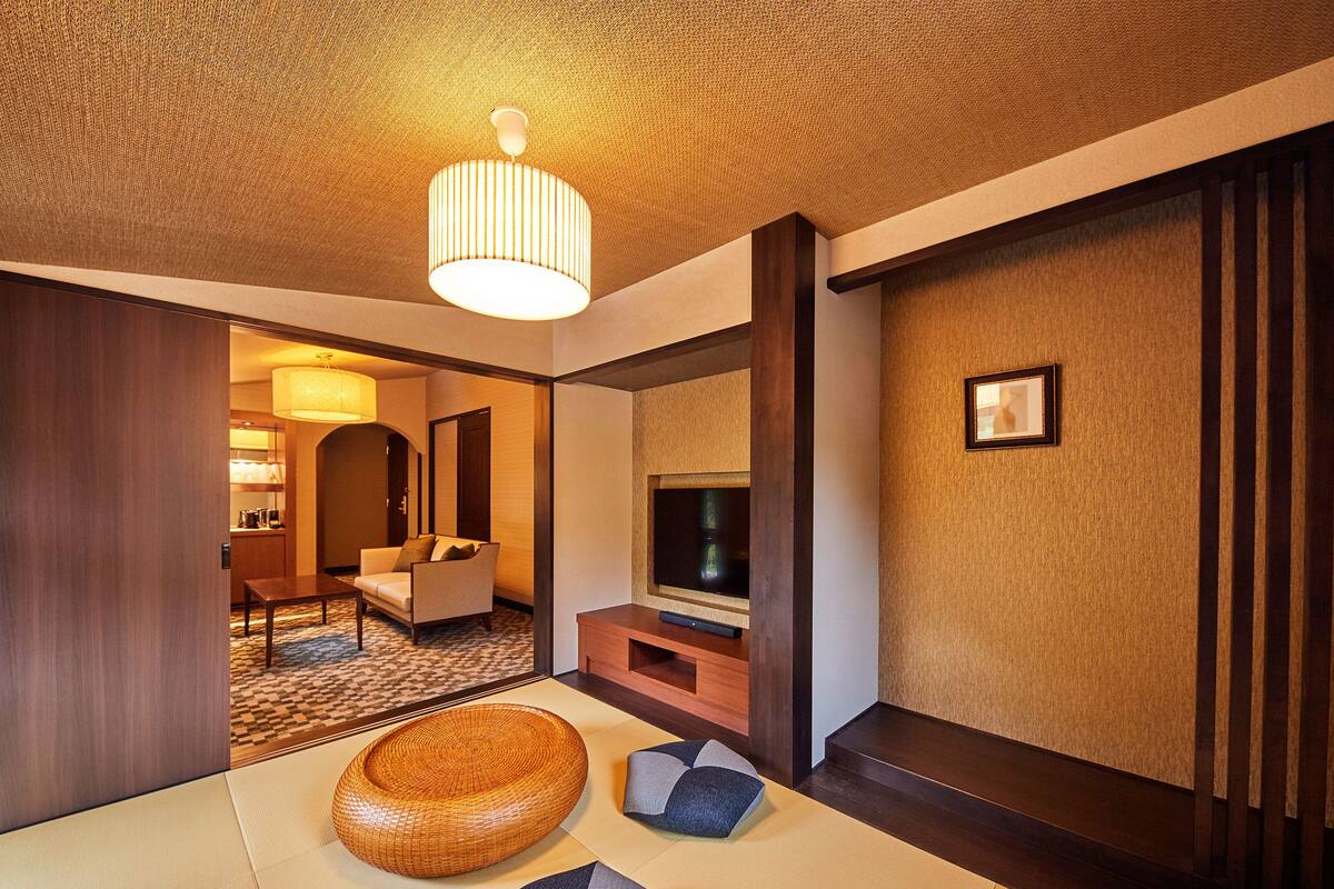 A hotel room with a traditional design, featuring tatami mats, a low wooden table, a sofa, and a television on a wooden stand.