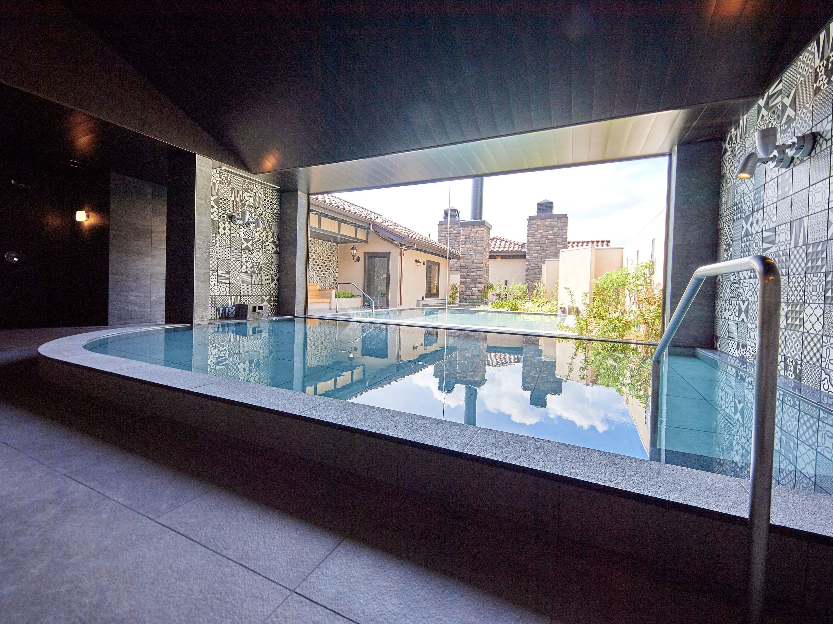 A modern indoor swimming pool with a glass barrier, stone walls, and a view of a residential area.