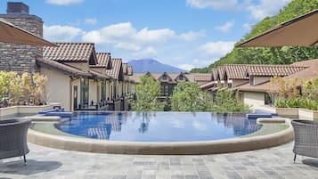 Uma área de piscina com vista desobstruída para as montanhas ao fundo, rodeada por edifícios com telhados de azulejo.