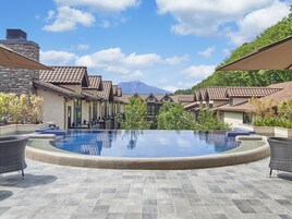 Zona de piscina con vista despejada a las montañas al fondo, rodeada de edificios con tejados de baldosas.