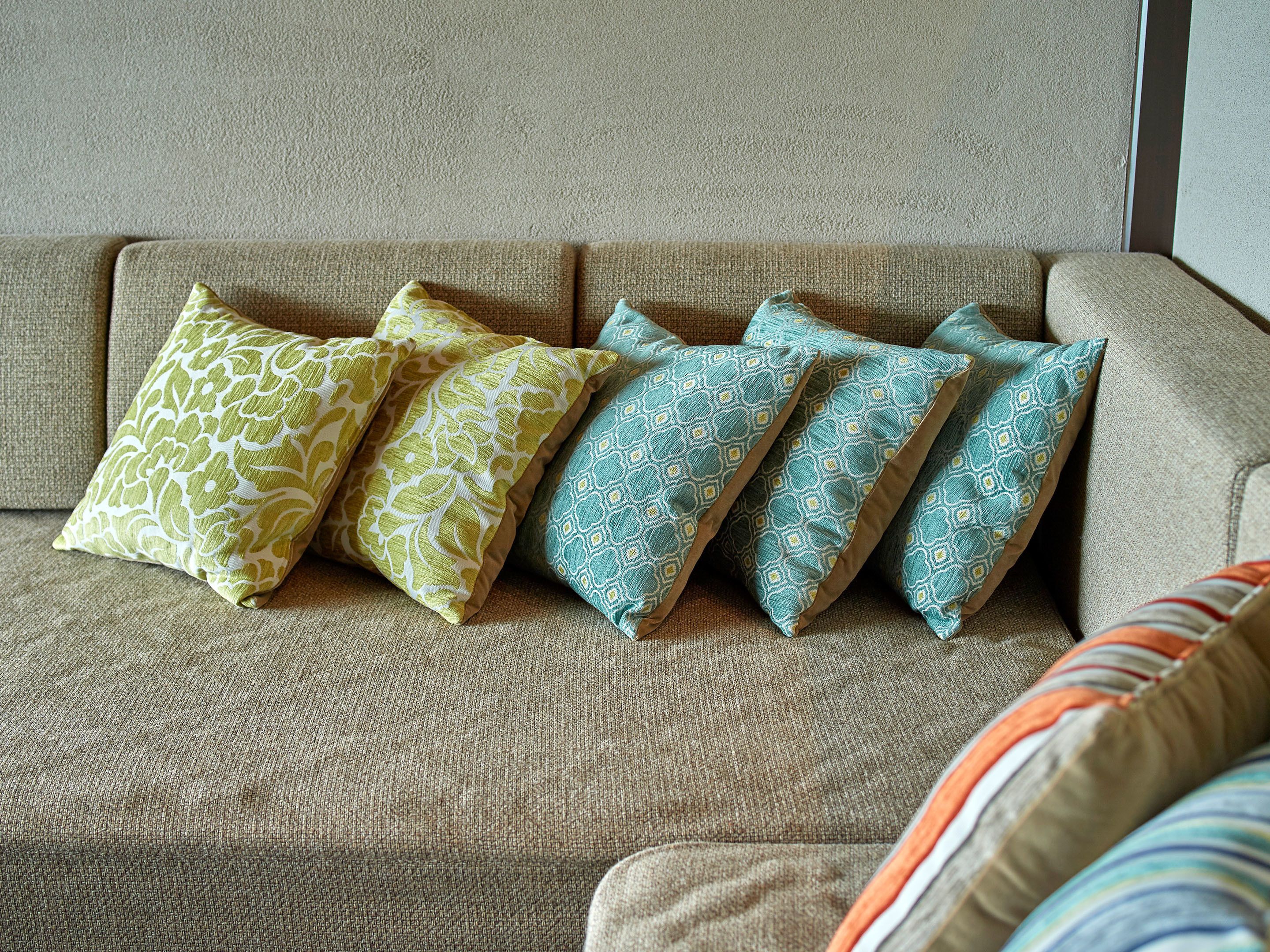 A beige sofa with four patterned cushions in green, yellow, and blue.