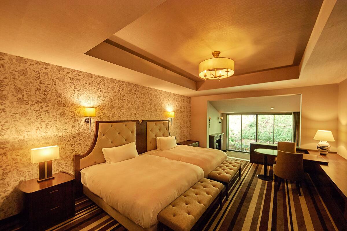 A hotel room with a large bed, two bedside tables, a desk with a chair, and a view of the outdoors.