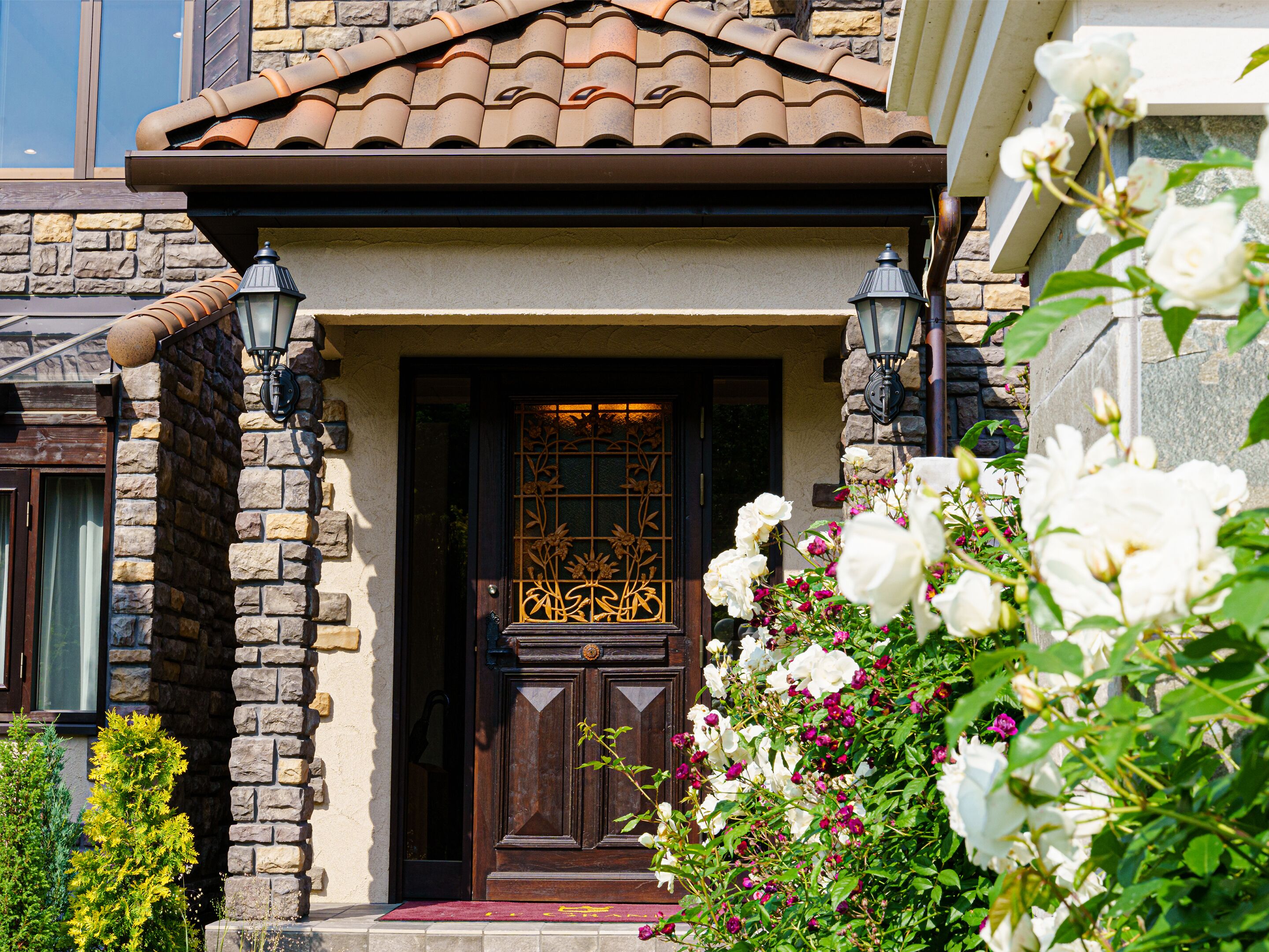 A stone facade with a wooden door, two wall-mounted lanterns, and a red mat at the entrance.