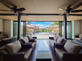 Amplio espacio interior con sofás de mimbre y una mesa de centro de vidrio, con vistas a una piscina y un complejo residencial.