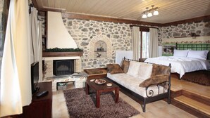 A cozy room with a stone fireplace, a bed with a green headboard, a wooden coffee table, and a stone wall. - Efharis Filoxenon (Sikyona)