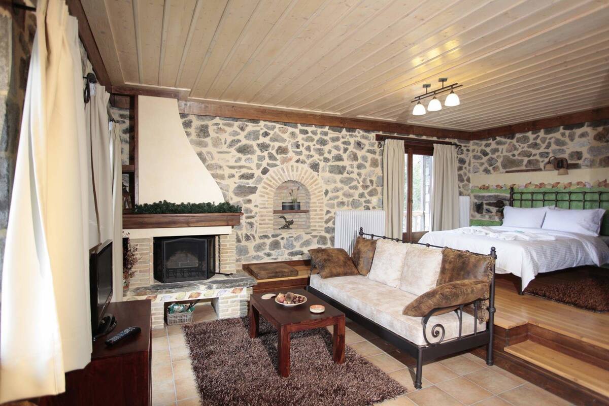 A cozy room with a stone fireplace, a bed with a green headboard, a wooden coffee table, and a stone wall.