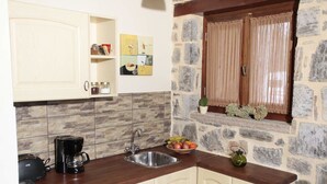A kitchen with stone walls, wooden cabinets, a sink, a coffee maker, and a window with curtains. - Efharis Filoxenon (Sikyona)