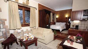 A cozy room with a bed, a sofa, a dining table with breakfast, a small kitchen, and a stone wall. - Efharis Filoxenon (Sikyona)