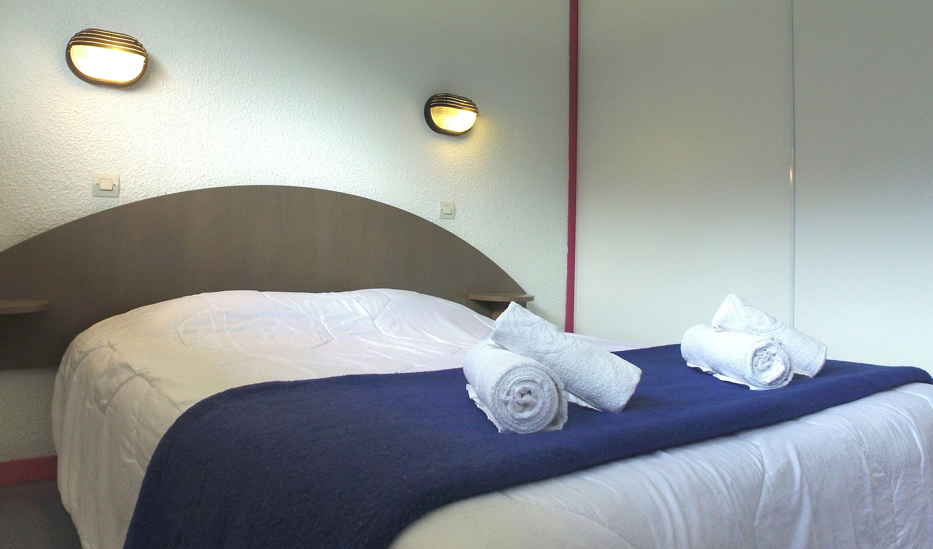 A hotel room with a bed, two wall-mounted lights, and a neatly made bed with towels.