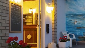 Een terras met een muurschildering, een houten deur en een menubord.
