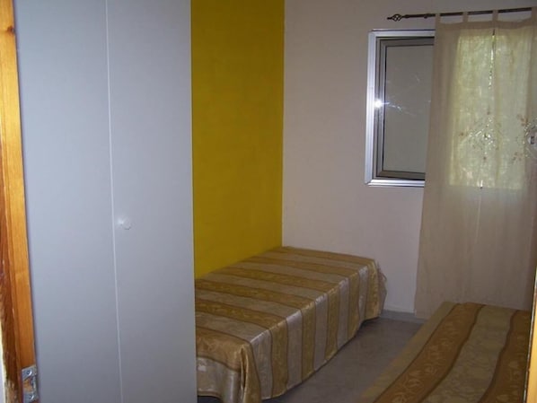 Une petite chambre avec un lit simple, une fenêtre avec un rideau et une porte.