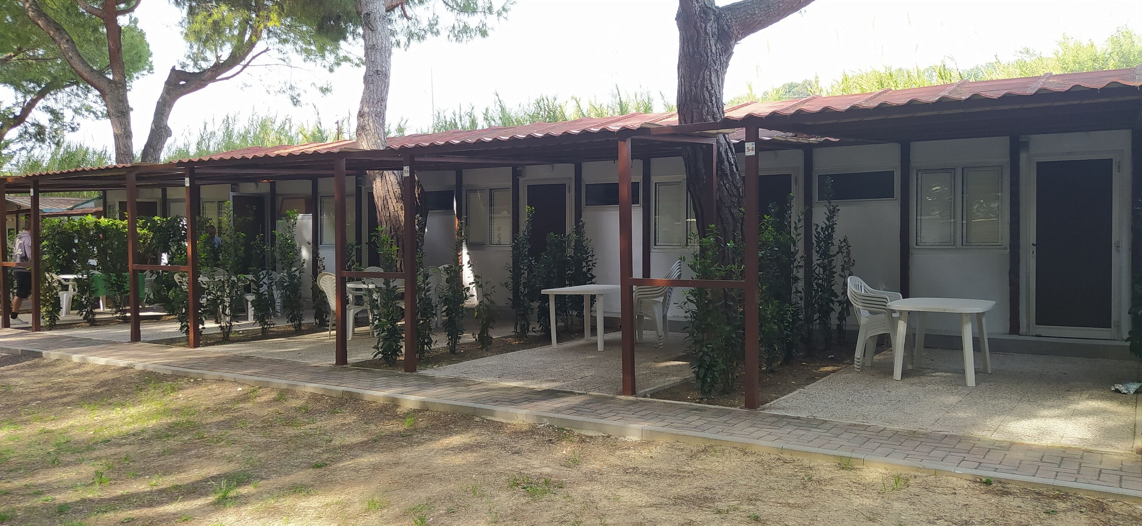 A covered outdoor seating area with tables and chairs, surrounded by trees and plants.