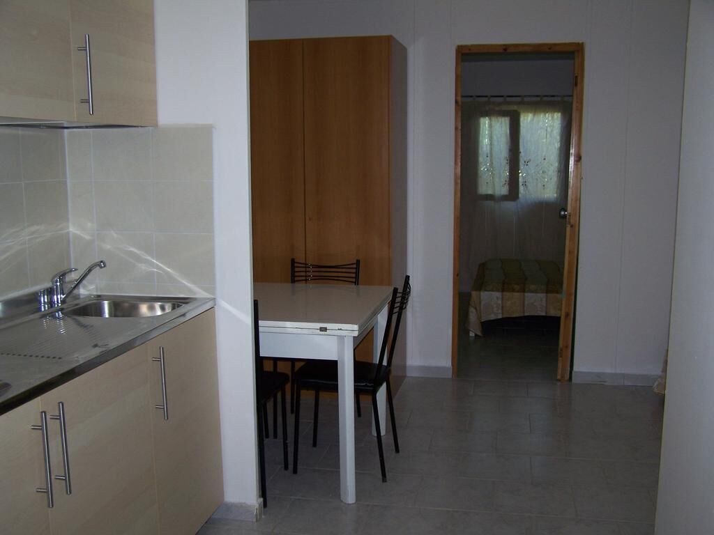 A compact kitchen with a dining area, a wooden wardrobe, and a small bedroom with a window.