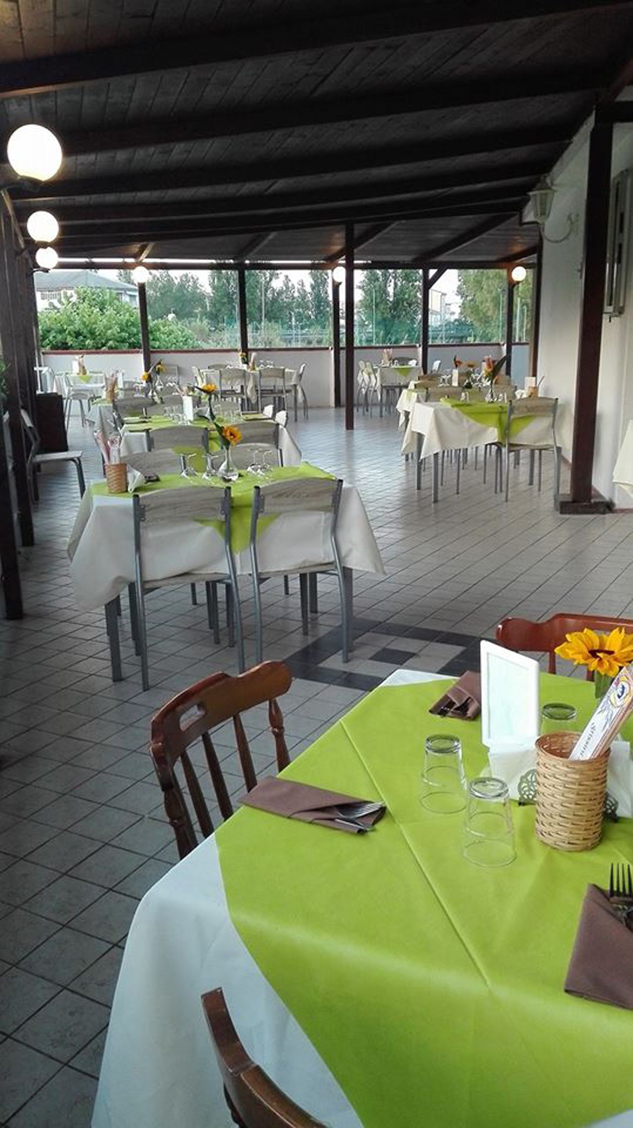 Un restaurante al aire libre con mesas cubiertas de manteles blancos y verdes, dispuestas en filas con sillas.