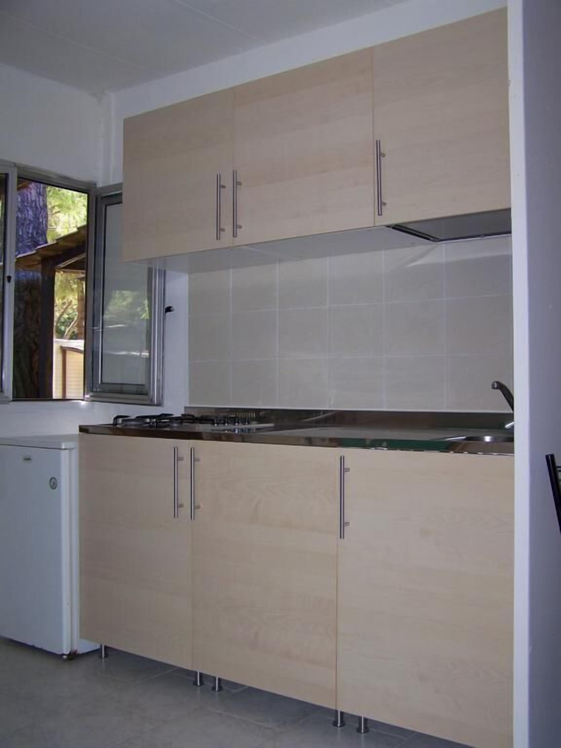 A kitchen with light wood cabinets, a white refrigerator, and a window with a view of greenery.