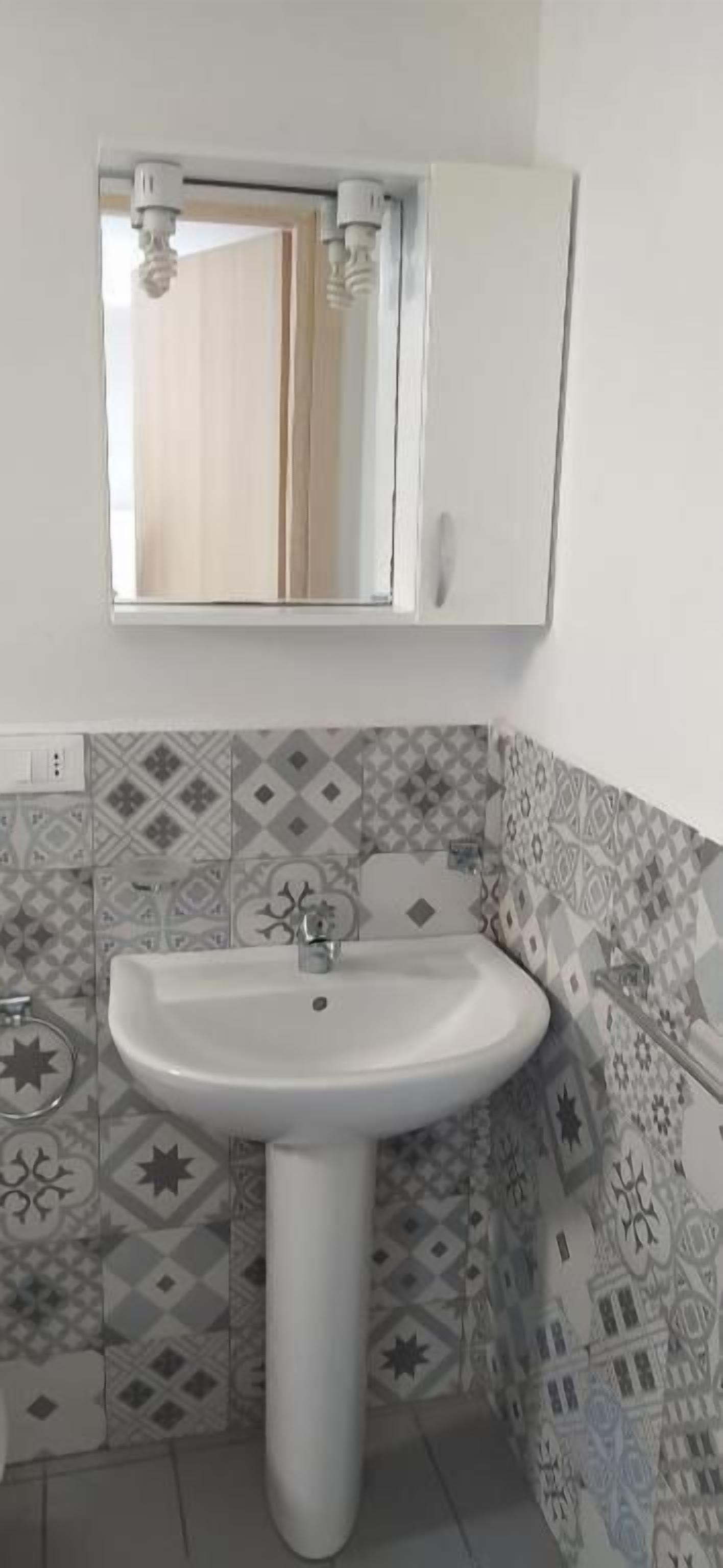 A bathroom with a white sink, patterned tiles, and a mirror above the sink.
