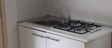Una cocina compacta con gabinetes blancos, estufa a gas y salpicadero de azulejos.