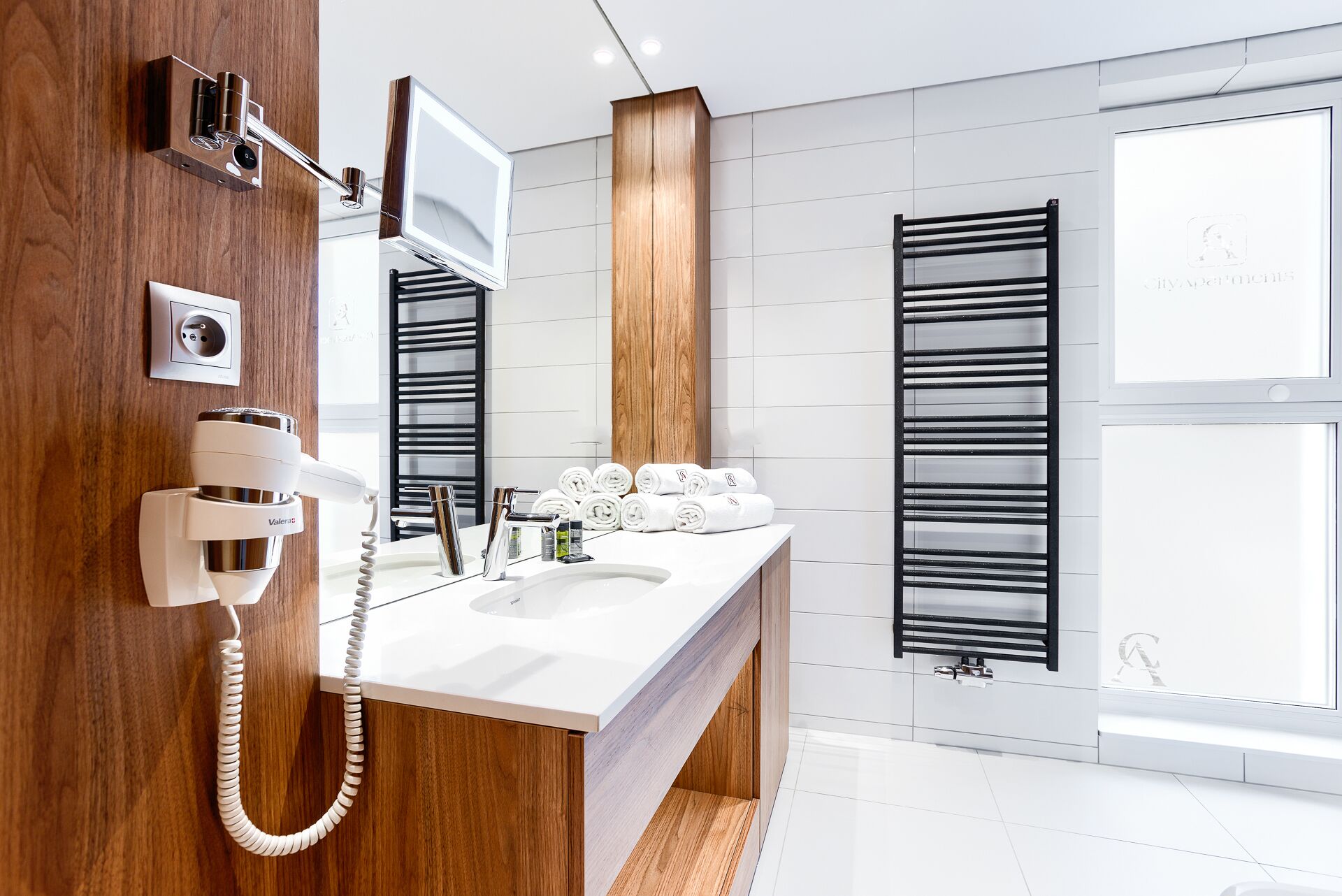 Une salle de bain moderne avec un meuble-lavabo en bois, un miroir encastré, un porte-serviettes et une fenêtre équipée de stores.