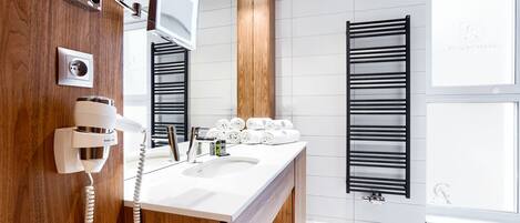 Une salle de bain moderne avec un meuble-lavabo en bois, un miroir encastré, un porte-serviettes et une fenêtre équipée de stores.
