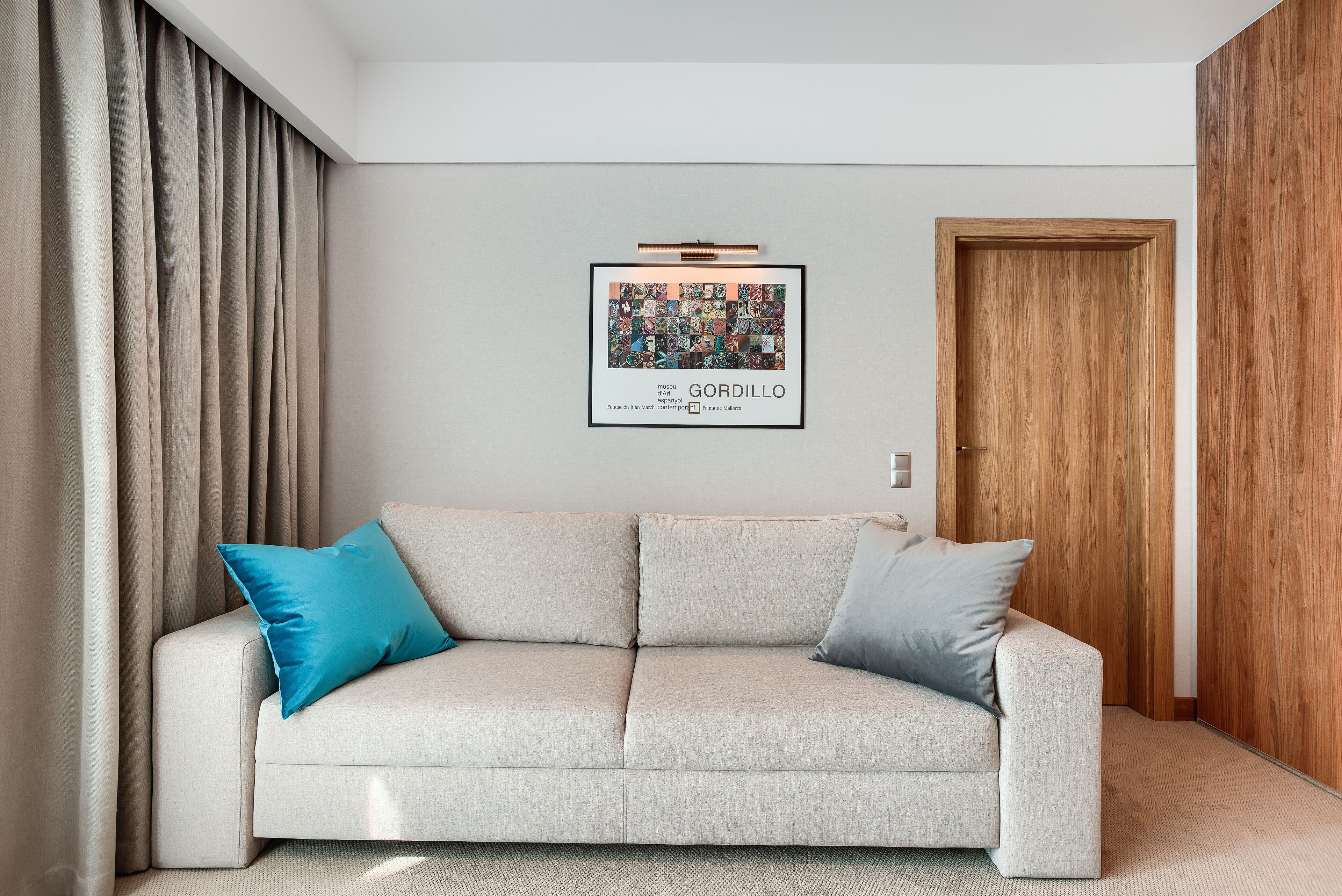 A neutral-colored sofa with two cushions, a framed artwork above it, and a wooden door to the right.