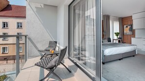 Een balkon met een stoel en tafel, een slaapkamer met een bed, nachtkastje en lamp.