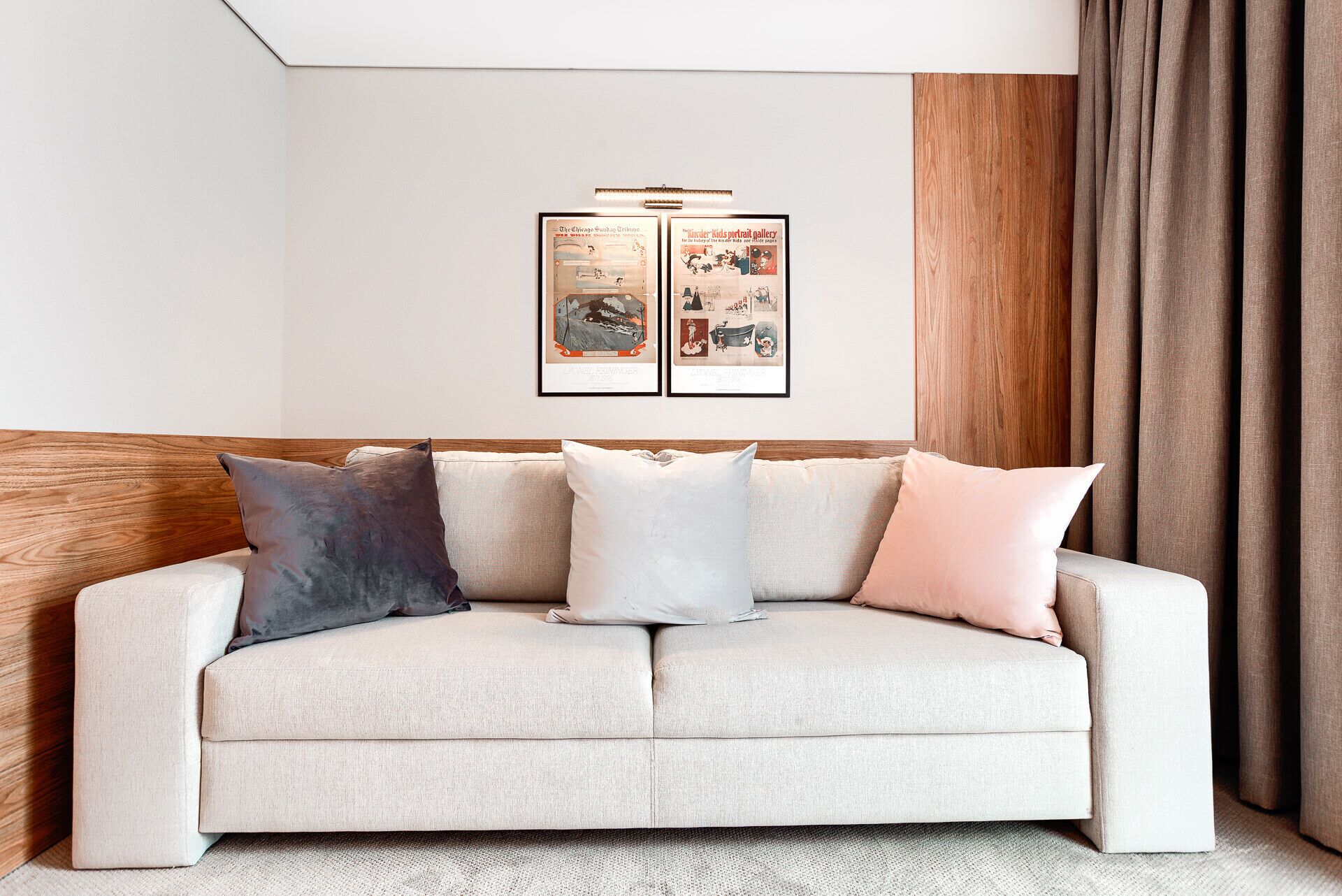 A living room with a beige sofa, three pillows, and two framed posters on the wall.