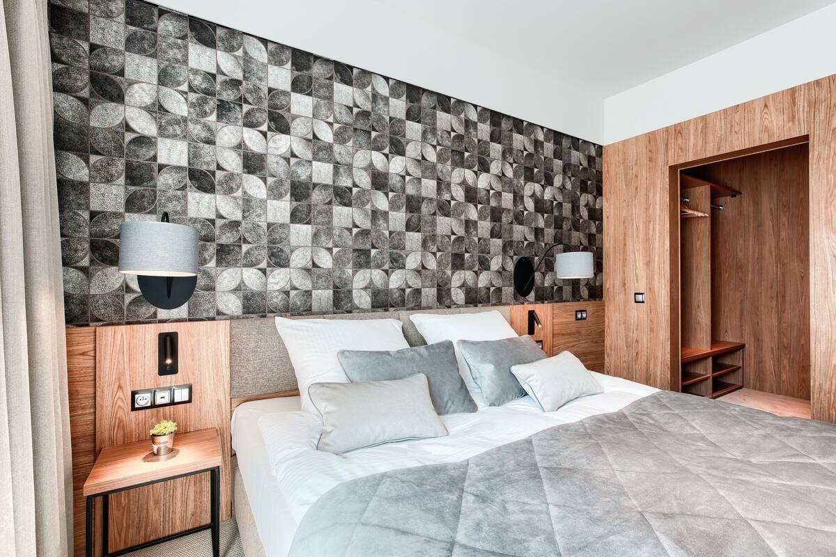 A modern bedroom with a geometric patterned headboard, a bedside table with a lamp, and a wardrobe.