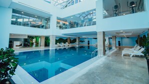 An indoor swimming pool with a glass ceiling, multiple levels, and lounge chairs around the pool area. - JRW Welmond Hotel & Casino Batumi (Batumi)