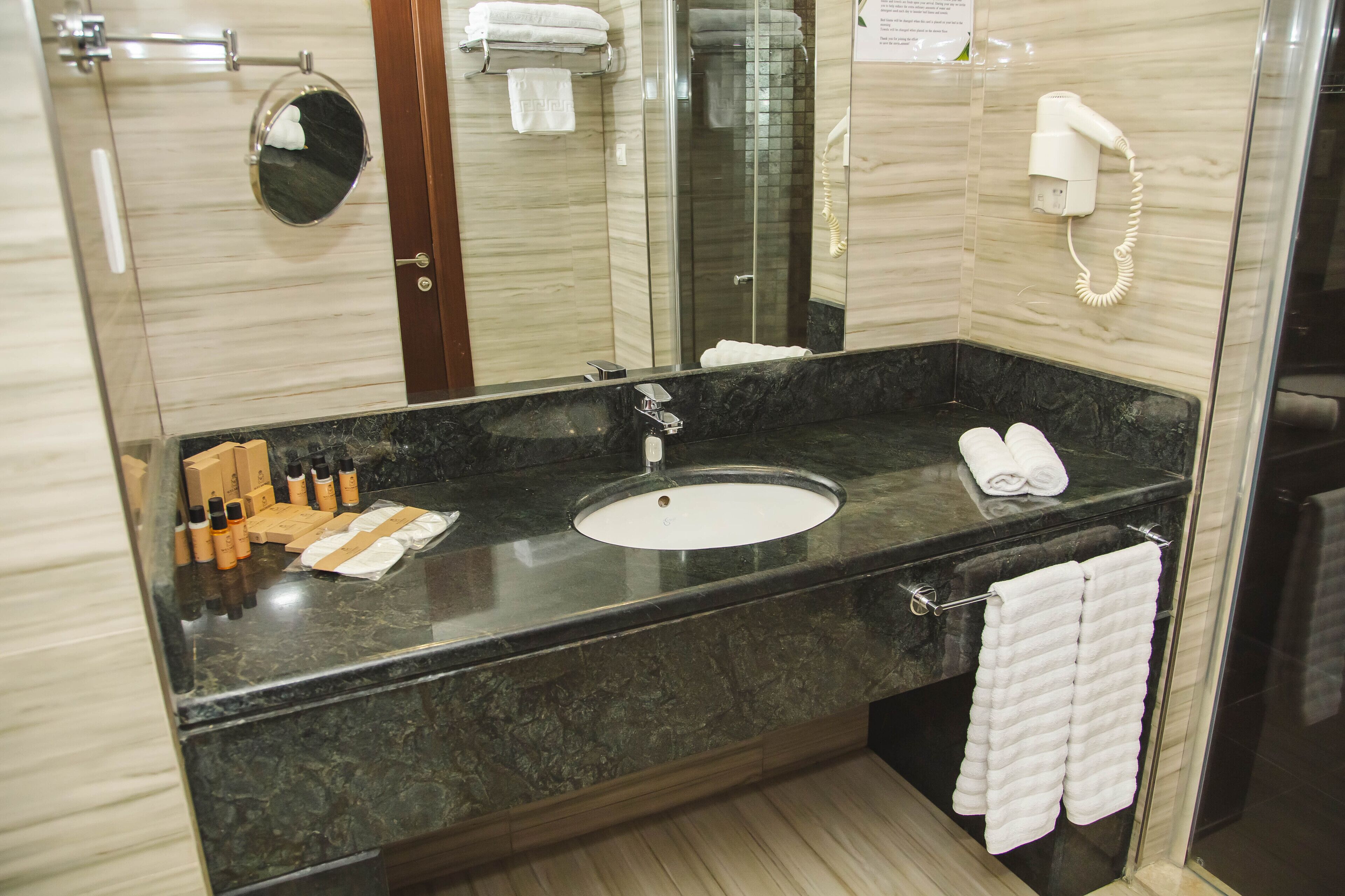 A modern bathroom with a marble sink, a glass-enclosed shower, and a hairdryer mounted on the wall.