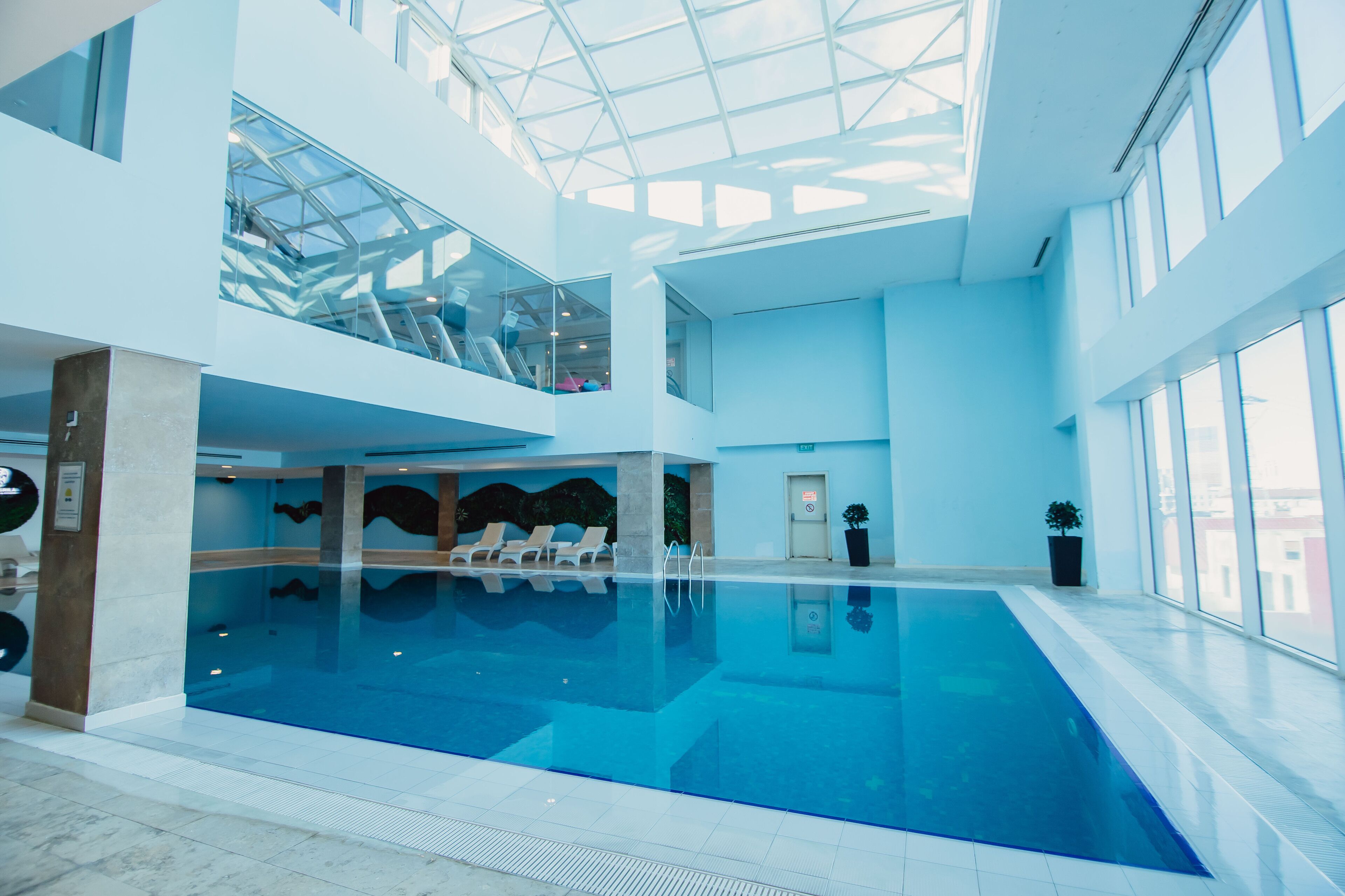 A large indoor swimming pool with clear glass ceilings, multiple levels, and a modern architectural design.